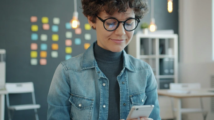 Woman in glasses holding a smartphone in office